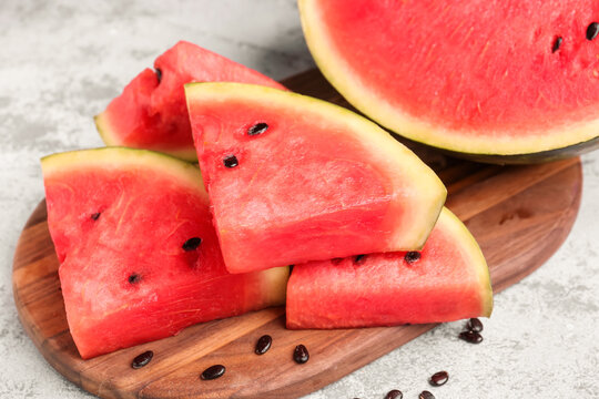 Board with pieces of fresh watermelon and seeds on grey background