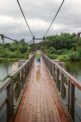 Fototapeta na wymiar Pedestrian bridge of complex and heavy metal structures. Light summer rain and tourist can admire the nature of Lithuania