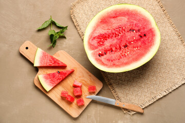 Half of fresh watermelon and board with pieces on brown background