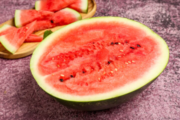 Half of fresh watermelon and board with pieces on purple background
