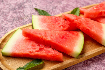 Board with pieces of fresh watermelon and mint on purple background