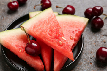 Plate with pieces of fresh watermelon and cherries on dark background