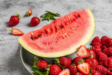 Plate with piece of fresh watermelon and different berries on grey background