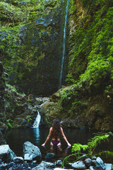 Tourist woman in bikini enjoys a refreshing bath in the pool at a picturesque overgrown waterfall in Madeira rainforest. Levada of Caldeirão Verde, Madeira Island, Portugal, Europe.