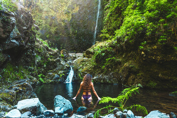 Tourist woman in bikini enjoys a refreshing bath in the pool at a picturesque overgrown waterfall...