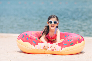 Lovely little child girl with two ponytails, wearing a stylish swimsuit lying on an inflatable...