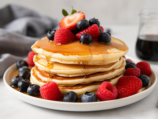 A stack of fluffy pancakes drizzled with maple syrup and topped with fresh berries.