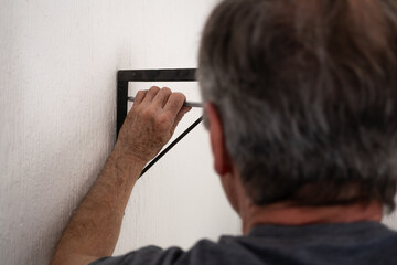 Hombre de edad mayor, atornillando una ménsula negra sobre pared blanca © AnaPliego