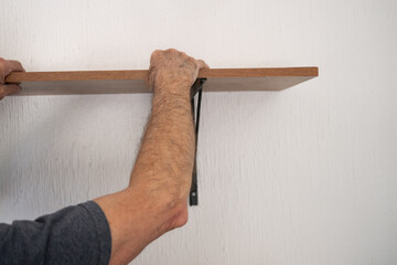 Hombre de edad mayor, instalando una repisa de madera sobre ménsula negra en pared blanca