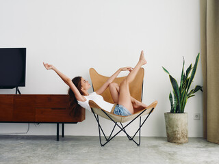 Woman lying in a leather armchair raised arms and legs cheerful happiness and a smile, relaxing at...