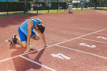 Young professional male athlete in blue sportswear taking a start position for a sprint run during outdoor training
