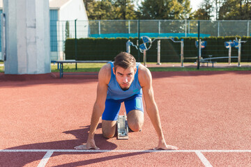 Front view of a Caucasian male sprinter in a race starting position, hands on the line and legs on...