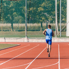 Fototapeta premium Caucasian male athlete in blue sportswear running alone along an athletic track on the stadium