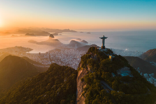 Rio de Janeiro, Brazil - June 10, 2023: Christ the Redeemer statue on top of the Corcovado Mountain with the Sugarloaf Mountain in the horizon on sunrise.