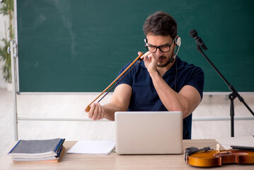 Young male music teacher sitting in the classroom
