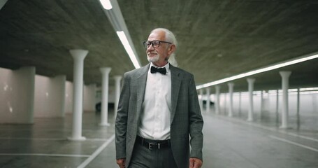 A gray-haired businessman walks through the parking lot to his car. A gray-haired man in a business castum goes to slow motion. An old man in a castum. - Powered by Adobe