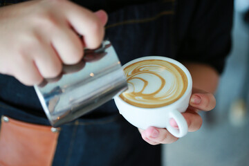 Barista hands pouring warm milk in coffee cup for making latte art. Multi skill of barista to make coffee drink in coffee shop. Profesional in hot and cold drink and ready to serve to the customer.