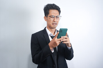 Asian guy wearing a suit looks sad reading online news from his cellphone. man shows disappointed gesture by wiping tears from his face