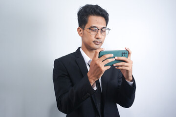 Portrait of a passionate and serious young man in suit playing game on mobile in office isolated over white background