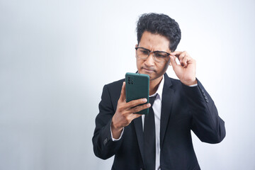 Portrait of handsome young adult with dreamy look, thinking while holding smartphone, isolated over white background.