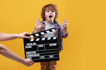 Emotional cute boy performing while second assistant camera holding clapperboard on orange...