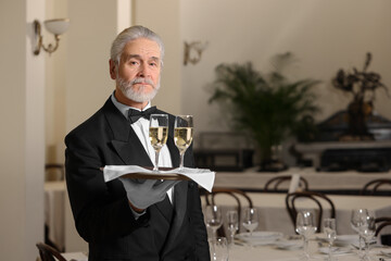 Senior butler holding tray with glasses of sparkling wine in restaurant. Space for text