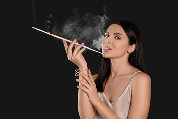 Obraz premium Woman using long cigarette holder for smoking on black background, space for text