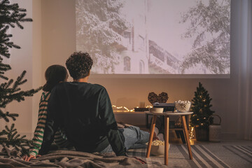 Couple watching Christmas movie via video projector at home, back view