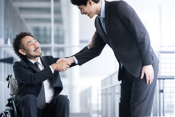 握手をするビジネスマン　車椅子に乗ったビジネスマンと迎える人