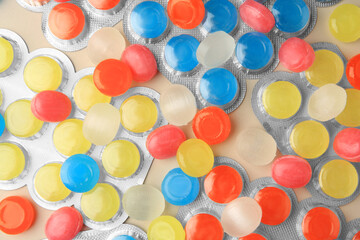 Blisters and many colorful cough drops on beige background, flat lay