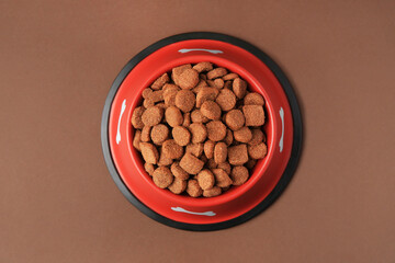 Dry dog food in feeding bowl on brown background, top view