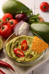 Bowl of delicious guacamole, nachos chip and ingredients on table