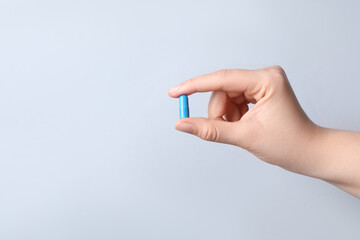 Woman with pill on light grey background, closeup. Space for text