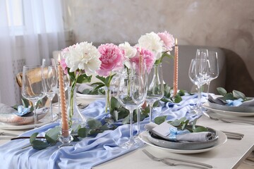 Beautiful table setting. Plates near glasses, peonies and cutlery on table in room