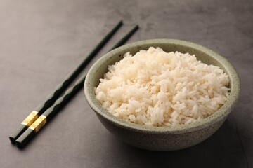 Delicious rice in bowl and chopsticks on grey table