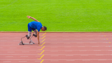 Asian speed runner on stadium track, alert and ready, anticipation building, geared to start his run