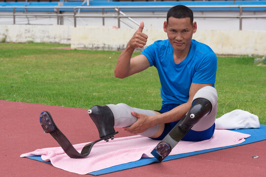 an Asian paralympic athlete, sporting two prosthetics running blades, presents a thumbs up, signaling readiness to start his training at the sports stadium