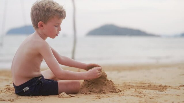 Boy Places A Rock On A Pile Of Sand On A Beach