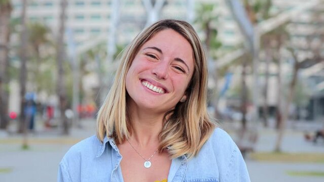 Individual portrait of happy blonde young adult woman standing outside with friendly and optimistic expression. Caucasian beauty female with perfect white teeth smiling and looking satisfed at camera