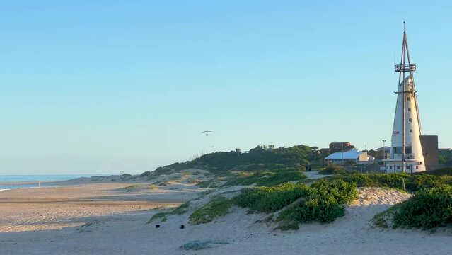 Glider flying by Jeffrey's Bay Lighthouse South Africa WSL JBAY Corona Open Supers Boneyard downtown main tourist beach late afternoon sunset mid summer slow motion pan to the left