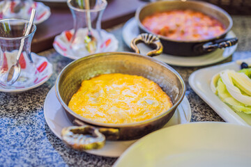 Turkish breakfast table. Pastries, vegetables, greens, olives, cheeses, fried eggs, spices, jams, honey, tea in copper pot and tulip glasses, wide composition