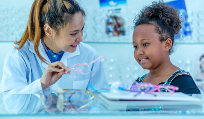 Young Asian woman optician suggests optical glasses frame and color to the young girl customer in...