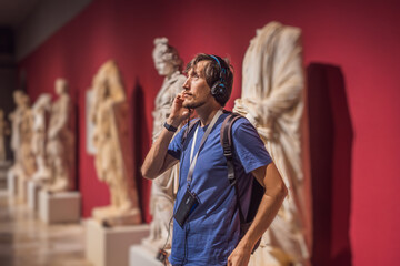 Fototapeta na wymiar Portrait of contemporary man looking at sculptures and listening to audio guide at museum exhibition