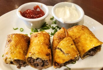 Cuts of cheesesteak rolls on a white plate with 2 dipping sauces