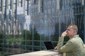Sad guy with hearing aid using laptop outdoors. 