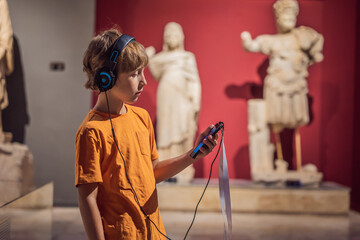Boy looking at sculptures and listening to audio guide at museum exhibition