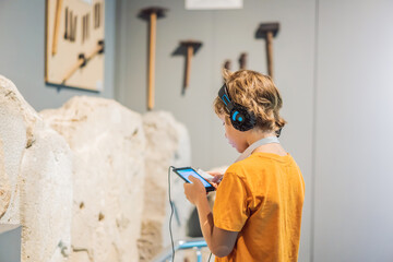 Boy looking at sculptures and listening to audio guide at museum exhibition - obrazy, fototapety, plakaty