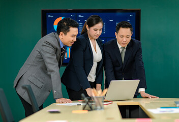 Millennial Asian professional successful male female businessmen and businesswoman in formal business suit standing smiling working discussing brainstorming via laptop together in office meeting room