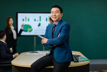 Millennial Asian professional successful businessman ceo entrepreneur in formal business suit smiling crossed arms smiling in meeting room with male and female colleagues discussing.