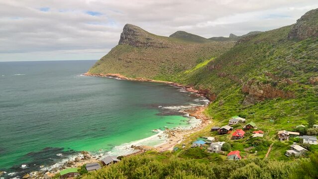 Smitswinkel Bay small beach town Cape of Good Hope most southern point large mountain cliffside coastline scenic South Africa Cape Town daytime beauty deep blue aqua lush summertime pan left
